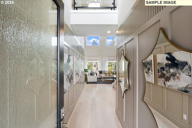 hallway with a towering ceiling, light wood finished floors, and a decorative wall