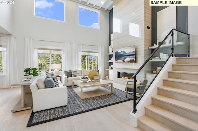 living area with a towering ceiling, a large fireplace, stairway, and light wood finished floors