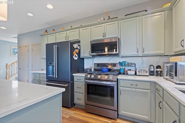 kitchen featuring light wood-type flooring, recessed lighting, backsplash, light stone countertops, and appliances with stainless steel finishes