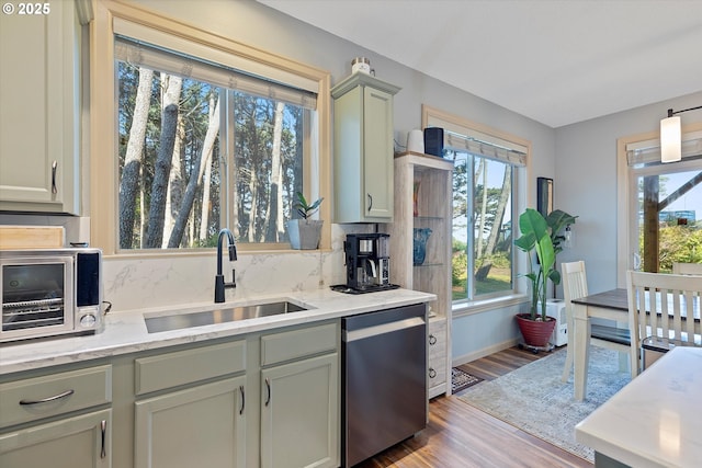 kitchen with light stone counters, decorative backsplash, dishwasher, a sink, and wood finished floors