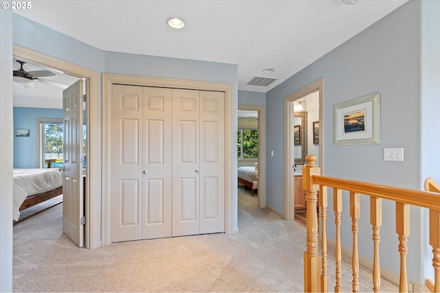 hall with light carpet, an upstairs landing, visible vents, and a healthy amount of sunlight