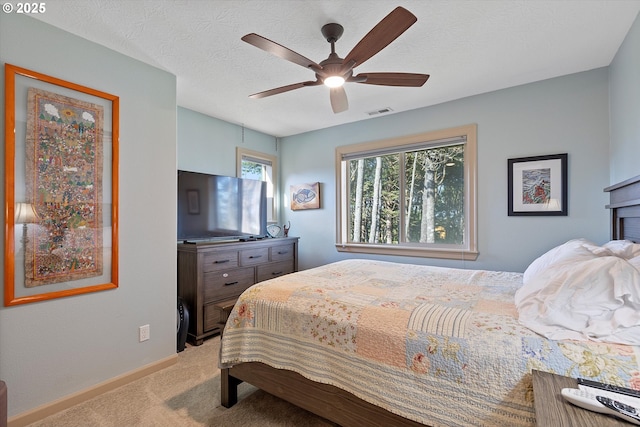 bedroom featuring baseboards, light carpet, a textured ceiling, visible vents, and ceiling fan