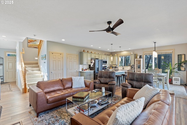 living area with light wood-style flooring, recessed lighting, a ceiling fan, and stairs