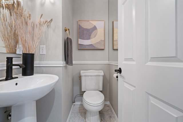 half bathroom with toilet, baseboards, and a sink