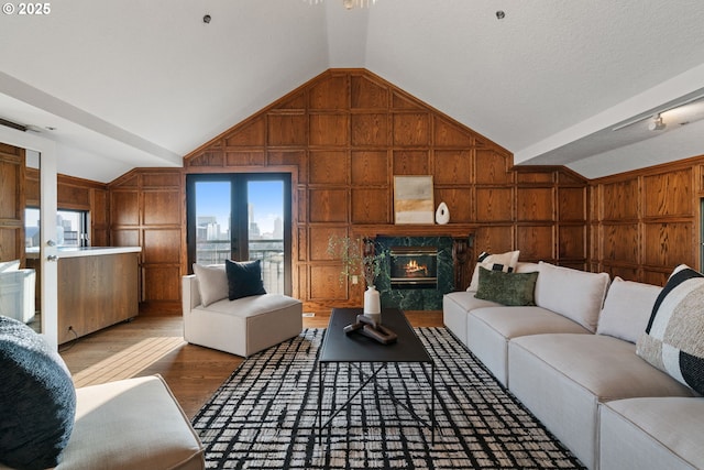 living room featuring wood finished floors, a premium fireplace, vaulted ceiling, wood walls, and a decorative wall