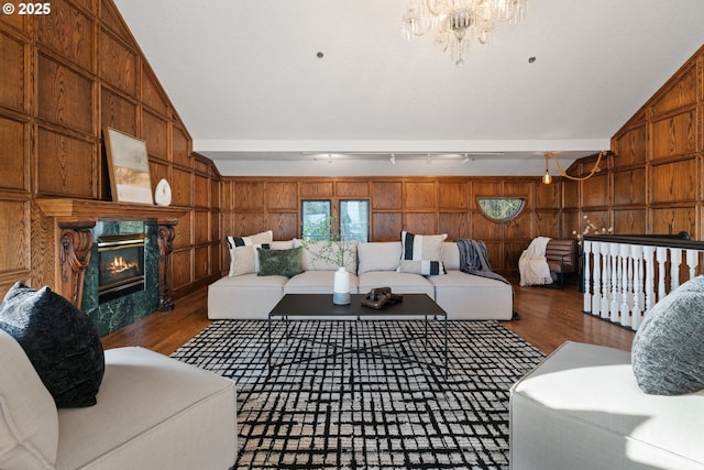 living room featuring wood finished floors, a premium fireplace, lofted ceiling, wood walls, and a notable chandelier