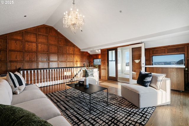 living area featuring vaulted ceiling, a notable chandelier, light wood finished floors, and wood walls