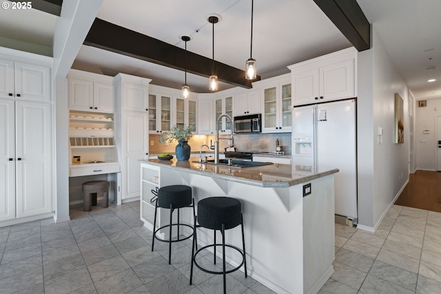 kitchen featuring stainless steel microwave, backsplash, beam ceiling, white refrigerator with ice dispenser, and white cabinetry