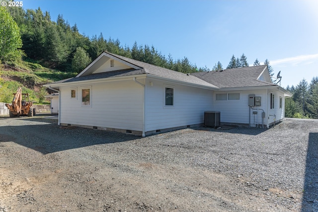view of home's exterior with crawl space, cooling unit, roof with shingles, and gravel driveway