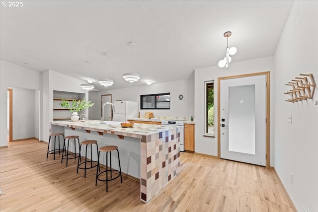 80487 Sha Ne Mah Rd, Seaside, OR 97138 - kitchen featuring white appliances, light wood finished floors, a kitchen breakfast bar, an island with sink, and decorative light fixtures
