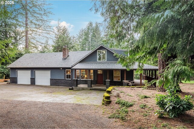 view of front facade featuring driveway, a chimney, an attached garage, covered porch, and brick siding