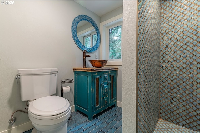 bathroom with a textured wall, toilet, vanity, baseboards, and walk in shower