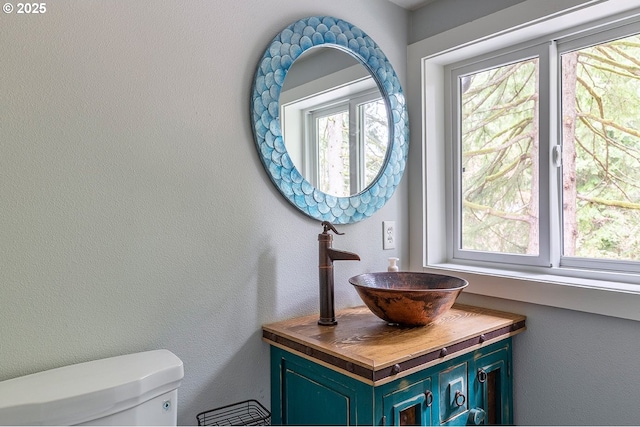 half bathroom with a textured wall, vanity, and toilet