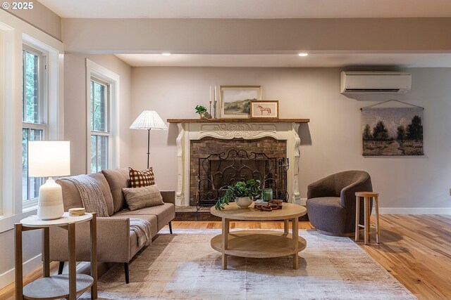 living area with baseboards, a fireplace with raised hearth, wood finished floors, a wall mounted AC, and recessed lighting