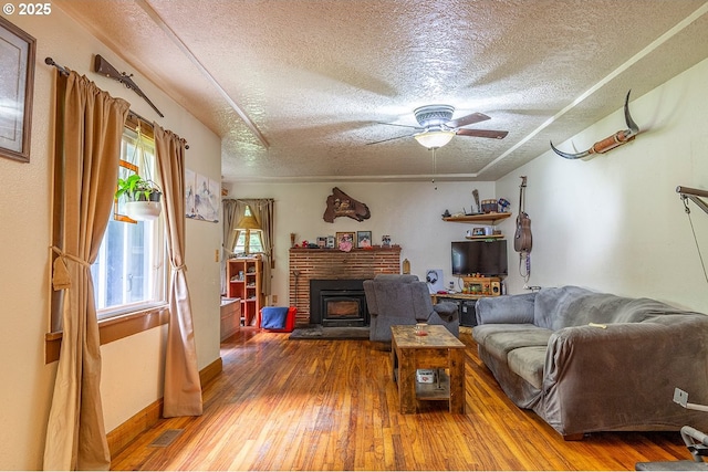 living room featuring a fireplace, wood-type flooring, visible vents, ceiling fan, and a textured ceiling