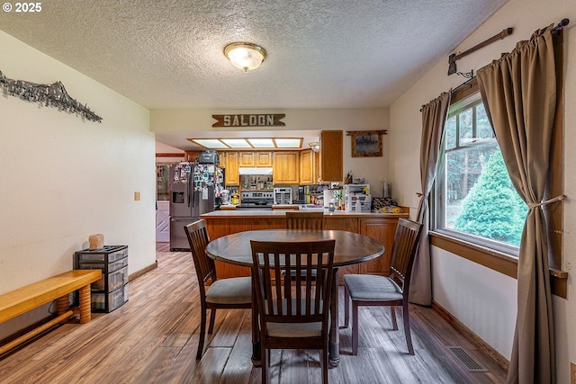 dining room featuring light wood-style floors, baseboards, visible vents, and a textured ceiling