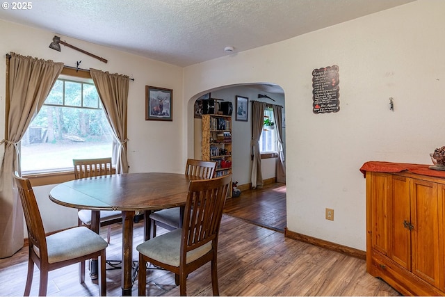 dining area with light wood-type flooring, arched walkways, a textured ceiling, and baseboards