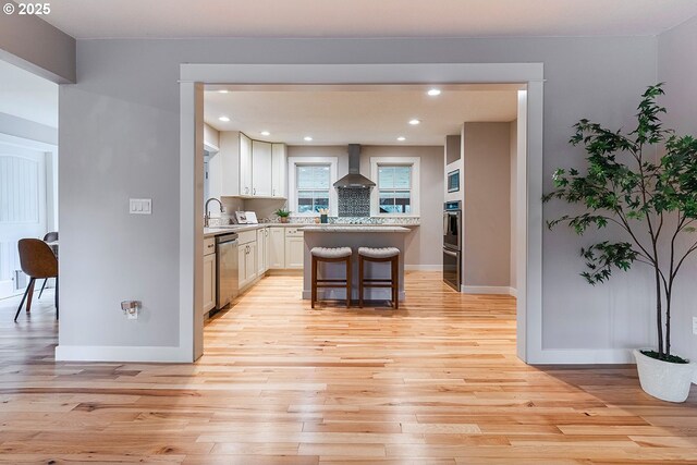 kitchen featuring stainless steel appliances, a kitchen island, light countertops, light wood-type flooring, and wall chimney exhaust hood