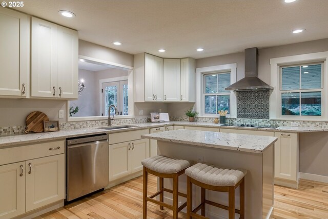 kitchen featuring black electric stovetop, a sink, wall chimney range hood, dishwasher, and light wood finished floors