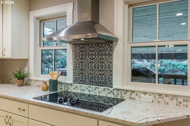 kitchen featuring light stone countertops, backsplash, wall chimney exhaust hood, and black electric cooktop