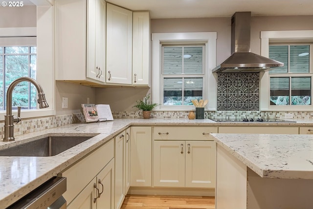 kitchen featuring black electric stovetop, stainless steel dishwasher, decorative backsplash, a sink, and wall chimney exhaust hood