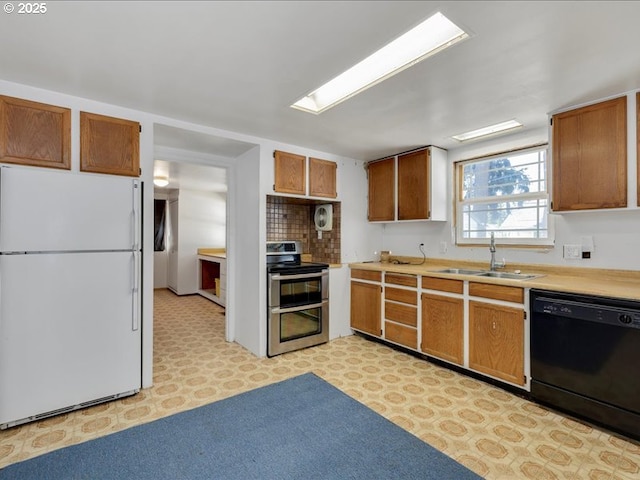kitchen featuring a sink, freestanding refrigerator, black dishwasher, double oven range, and light floors