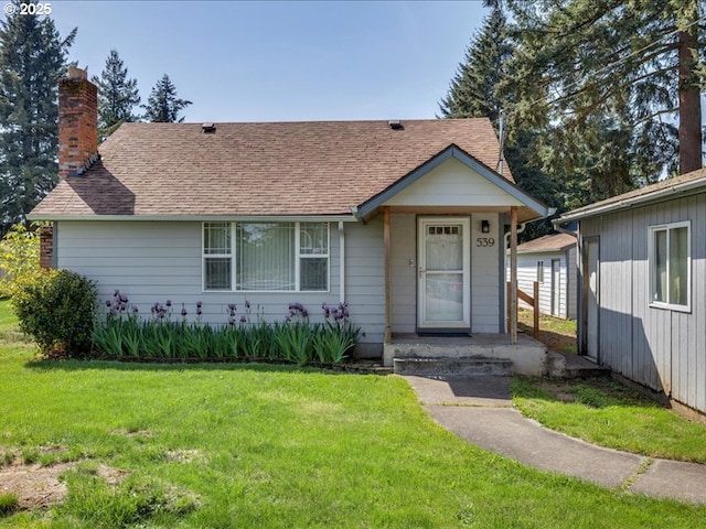 view of front of property with roof with shingles, a chimney, and a front yard