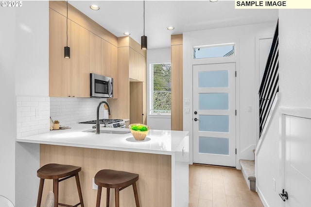 kitchen with stainless steel microwave, a breakfast bar, light brown cabinetry, and light countertops