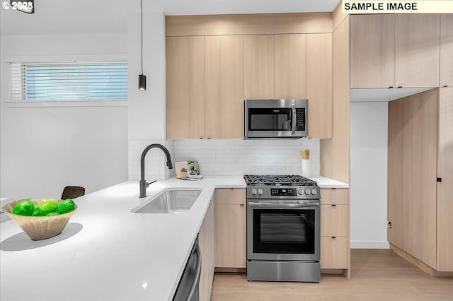 kitchen with modern cabinets, light brown cabinetry, a sink, appliances with stainless steel finishes, and light countertops