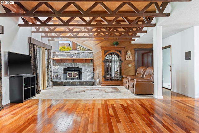 unfurnished living room featuring hardwood / wood-style flooring, baseboards, a stone fireplace, wooden walls, and beam ceiling