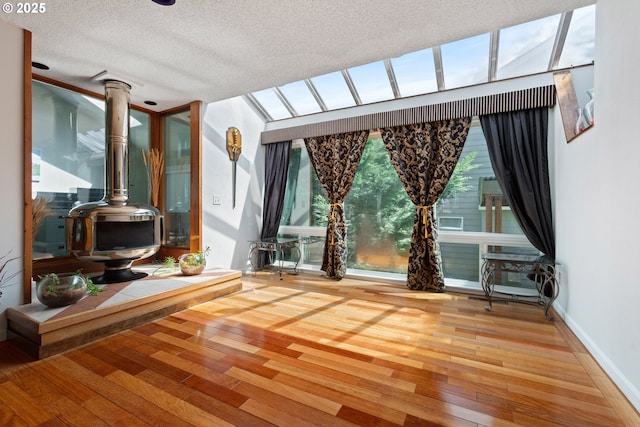 unfurnished room featuring hardwood / wood-style floors, a wood stove, a textured ceiling, and baseboards