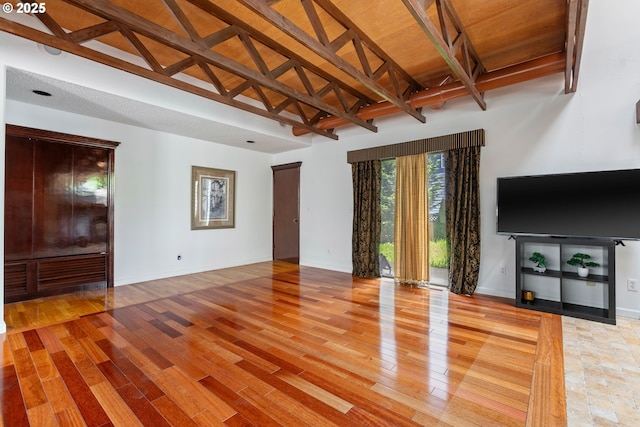 unfurnished living room featuring baseboards, beamed ceiling, light wood-style floors, and high vaulted ceiling