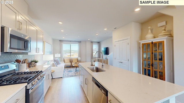 kitchen with appliances with stainless steel finishes, a kitchen island with sink, sink, and white cabinets