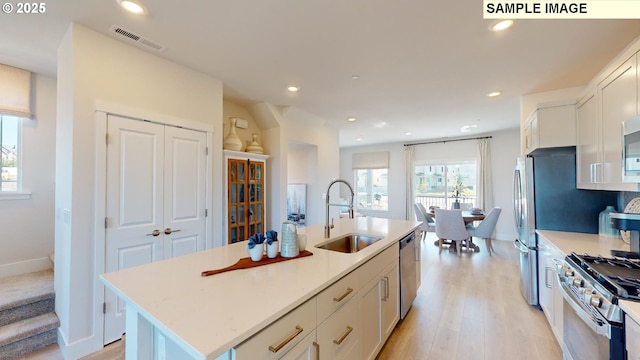 kitchen featuring appliances with stainless steel finishes, white cabinetry, an island with sink, sink, and light hardwood / wood-style flooring