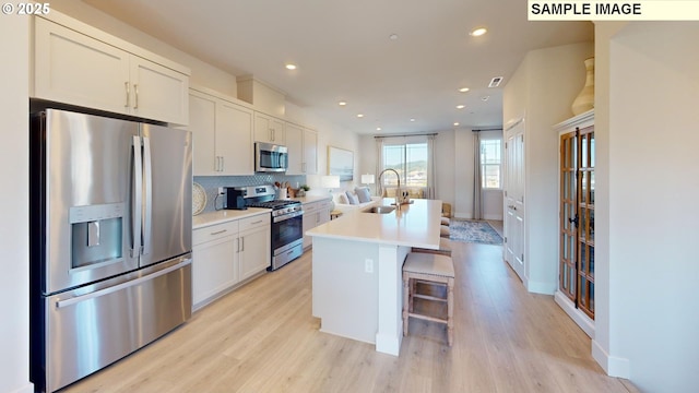 kitchen featuring sink, white cabinetry, appliances with stainless steel finishes, a kitchen breakfast bar, and a kitchen island with sink