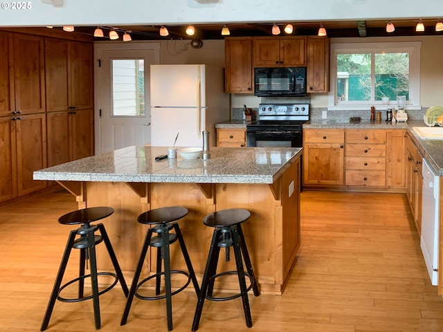 kitchen with a center island, a kitchen bar, black appliances, and light hardwood / wood-style flooring