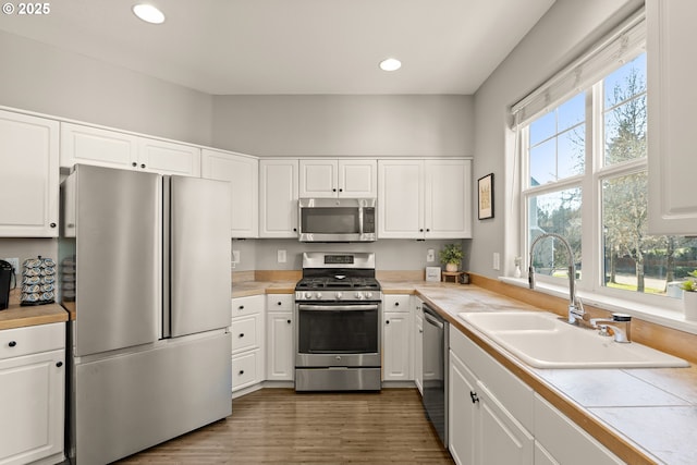 kitchen with sink, appliances with stainless steel finishes, white cabinetry, dark hardwood / wood-style flooring, and tile countertops