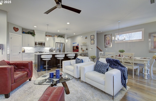 living room with ceiling fan with notable chandelier and light hardwood / wood-style floors