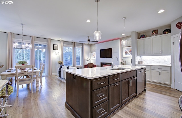 kitchen with sink, white cabinetry, decorative light fixtures, stainless steel dishwasher, and light wood-type flooring