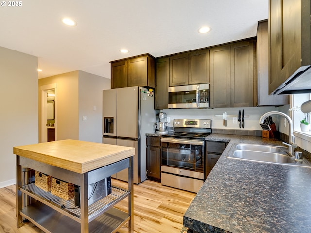 kitchen featuring stainless steel appliances, dark countertops, light wood-style floors, a sink, and dark brown cabinetry