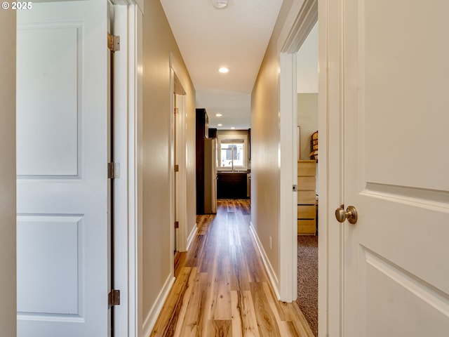 hall featuring recessed lighting, a sink, light wood-style flooring, and baseboards