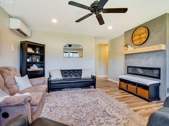 living area featuring recessed lighting, wood finished floors, baseboards, a wall mounted AC, and a glass covered fireplace