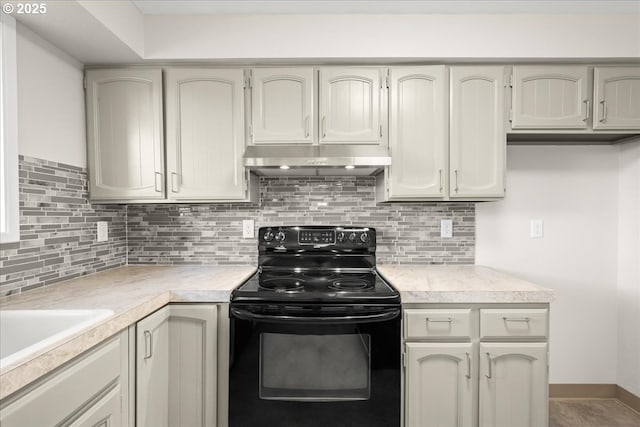 kitchen featuring black / electric stove, light countertops, decorative backsplash, under cabinet range hood, and baseboards