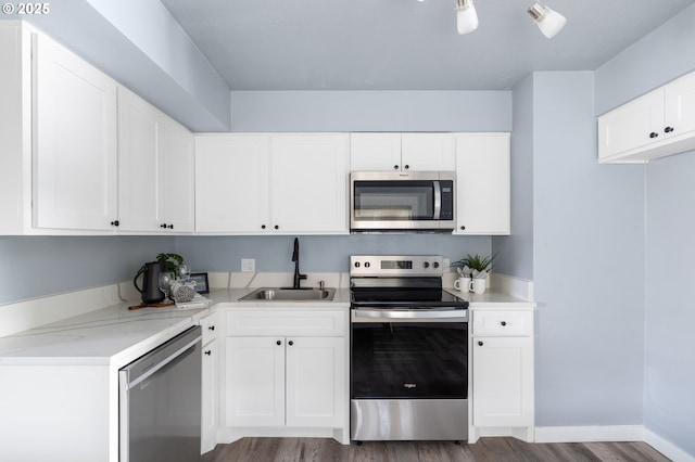 kitchen with appliances with stainless steel finishes, white cabinetry, sink, hardwood / wood-style flooring, and light stone countertops