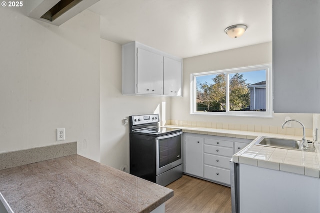 kitchen with stainless steel electric range oven, sink, tile countertops, white cabinets, and light wood-type flooring