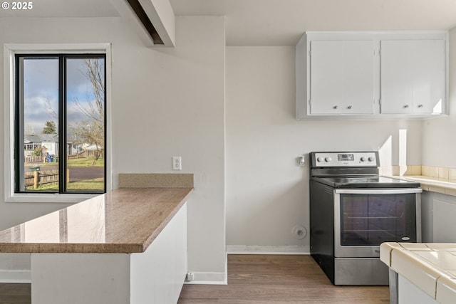 kitchen featuring kitchen peninsula, stainless steel range with electric stovetop, beamed ceiling, white cabinets, and hardwood / wood-style floors