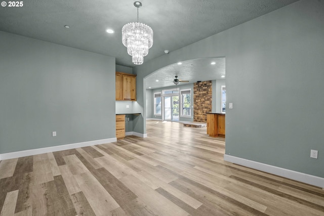 unfurnished living room featuring ceiling fan with notable chandelier, a textured ceiling, and light hardwood / wood-style flooring