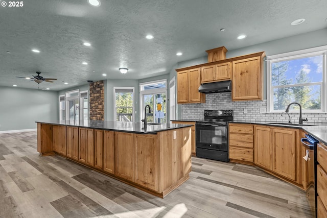 kitchen with light hardwood / wood-style flooring, a center island with sink, backsplash, and black appliances