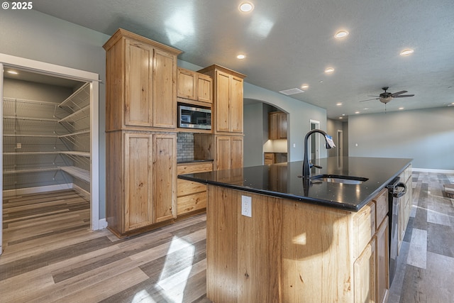 kitchen featuring sink, light wood-type flooring, stainless steel microwave, ceiling fan, and a kitchen island with sink