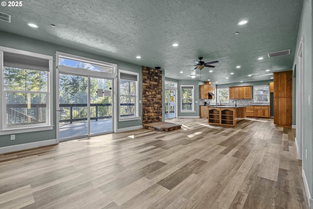 unfurnished living room featuring ceiling fan, sink, light hardwood / wood-style flooring, and a textured ceiling